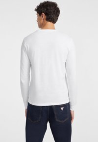 Balta ilga rankovėmis marška, pagaminta iš medvilnės, turinti paprastą dizainą. Dėvima kartu su tamsiais džinsais, demonstruojančiais reguliarią figūrą ir lygią tekstūrą.