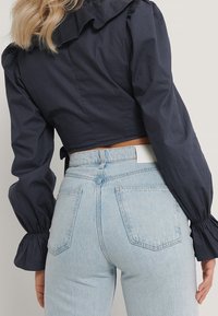 Blusa corta blu navy con colletto arricciato, in tessuto leggero. Abbinata a jeans in denim azzurro chiaro a vita alta con due tasche posteriori.
