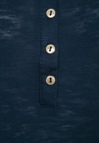 Marineblaue Strickware mit vier goldenen Knöpfen, die ein Schlüssellochdesign aufweist. Nahaufnahme des Textils und der Knopfdetails.