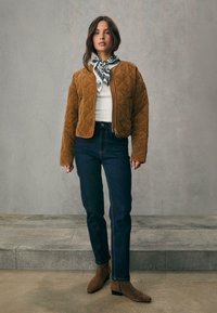 Brun manchesterquiltad jacka med dragkedja, kombinerad med mörkblå h�ögmidjade jeans och bruna mocka ankelstövlar. Svart-vit bandana.