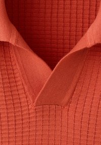 Gros plan d’un pull en maille rouge présentant un motif quadrillé texturé et un col en V plié.
