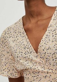 Vaaleanpunaisesta kankaasta valmistettu kukkakuosinen kietaisupaita, jossa on mustia ja keltaisia kuvioita, lyhyet hihat ja syvä V-pääntie. Päällä on teksturoidun pinnan viimeistely.