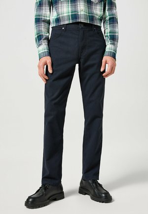 Pantaloni blu scuro dal taglio slim, realizzati in tessuto intrecciato. Presentano tasche anteriori e una vita pulita, abbinati a scarpe nere.