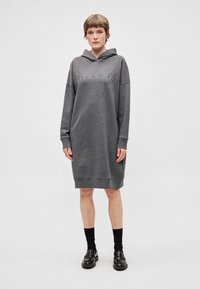 Šedé šaty s kapucí a elastickými manžetami a lemem, s vyšitým textem "Marc O'Polo" na přední straně. Hladká, měkká textura.