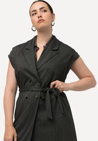 Grau gestreiftes ärmelloses Vest mit tiefem V-Ausschnitt, doppelten Knöpfen und Taillengürtel. Hergestellt aus strukturiertem Stoff mit taillierter Passform.