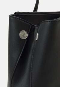 Intérieur d'un sac fourre-tout en cuir synthétique noir, doté d'une fermeture éclair et d'un bouton-pression magnétique. Texture lisse avec des accents en métal argenté.