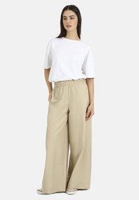 White short-sleeve t-shirt, relaxed fit, paired with beige high-waisted wide-leg trousers with an elastic waistband. Flat shoes visible.