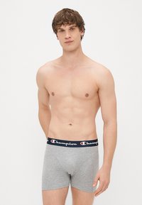 Boxer-briefs en coton gris avec une taille navy ornée du logo "Champion" en blanc. Le design est ajusté et a une texture lisse.