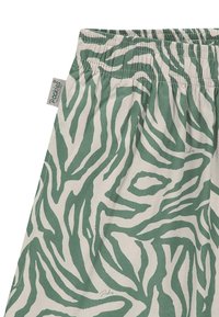 Bavlněná látka se vzorem zebra v zelené a béžové barvě, s nařaseným elastickým pasem a malou značkovou štítkem pečlivě připevněným.