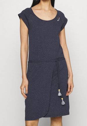 Mujer con vestido de manga corta a rayas azul marino, con cintura ajustable con cordón y detalles de borlas en el cinturón y el hombro.