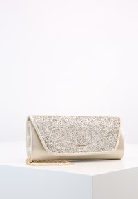 Lille gul clutch taske med glitrende frontlåg og tynd guld kæde-rem, vist på en hvid pedestal mod en lys baggrund.