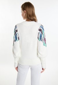 Witte, fluffy trui met pofmouwen; voorzien van kleurrijke, glinsterende accenten in blauw, groen en paars op de schouders; geribbelde zoom.