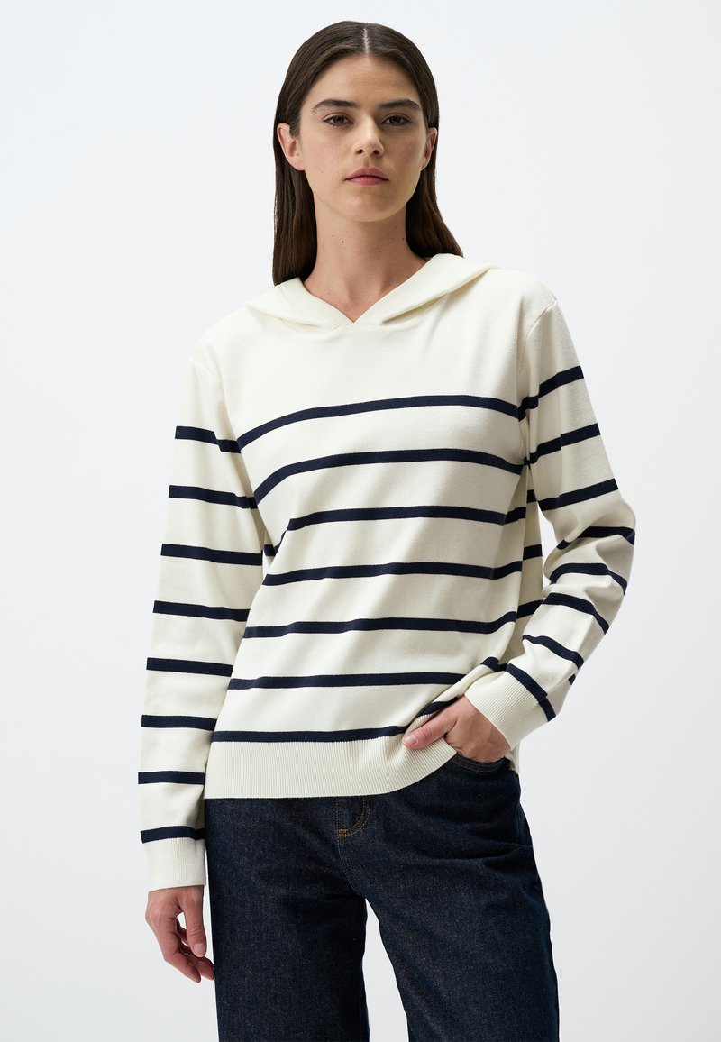 Gestreifter Kapuzenpullover in Creme mit marineblauen Streifen, mit V-Ausschnitt, langen Ärmeln und lockerer Passform, kombiniert mit dunkelblauen Jeans.