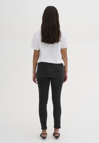 Jeans ajustados negros con bolsillos traseros, combinados con una camiseta blanca de manga corta. El largo y lacio cabello del modelo cae sobre los hombros.
