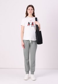 White t-shirt with graphic print, light gray joggers, and white sneakers. The model holds a black structured tote bag with straps.