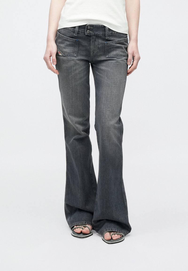 Άτομο που φοράει ξεθωριασμένο μαύρο τζιν bootcut με μπροστινές τσέπες και ασημένια σανδάλια, στέκεται μπροστά σε απλό λευκό φόντο.