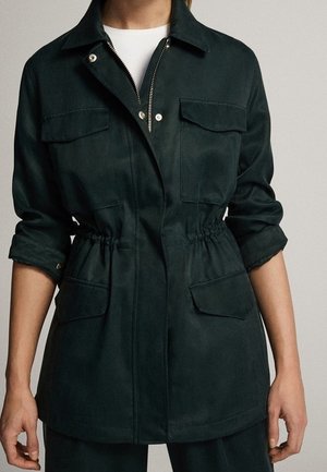 Ciemnozielona kurtka z zamkiem błyskawicznym z przodu i zatrzaskami, elastycznym pasem, podwiniętymi rękawami oraz dużymi kieszeniami z klapami na piersi i biodrach.