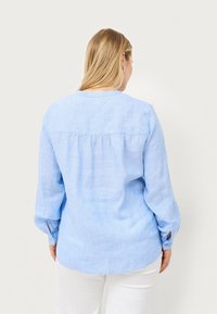 Chemise à manches longues bleu clair en lin. Dotée d'un dos froncé, d'un col rond et de poignets boutonnés. Texture lisse et coupe décontractée.