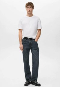 Biała koszulka z krótkim rękawem w połączeniu z ciemnoniebieskimi dżinsami o prostych nogawkach oraz czarnymi butami. Strój charakteryzuje klasyczny, casualowy design i fason.