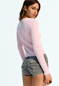 Geribbelde lichtroze top met lange mouwen, gecombineerd met grijze denim high-waisted shorts met ritszakken en decoratieve stiksels.
