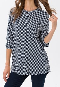 Blusa a pois blu navy e bianca con colletto rotondo, chiusura a bottoni e maniche a tre quarti. Tessuto morbido con una vestibilità comoda.