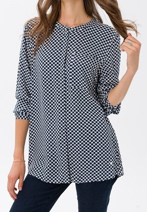 Blusa a pois blu navy e bianca con colletto rotondo, chiusura a bottoni e maniche a tre quarti. Tessuto morbido con una vestibilità comoda.