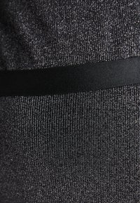 Black textured fabric with metallic threads, featuring a contrasting black satin waistband. Close-up view highlights material and design details.