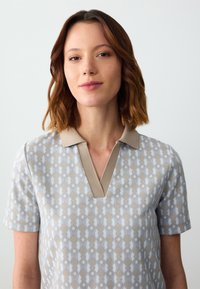 Lichtgrijze polo met een diamantpatroon in beige en blauw, met een zachte beige kraag en korte mouwen.