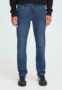 Donkerblauwe denim jeans met een rechttoe-rechtaan ontwerp, voorzakken en subtiele stikseldetails. Gecombineerd met zwarte sportschoenen.