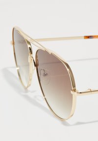 Occhiali da sole aviator dorati con lenti marroni graduali, montatura in metallo sottile e design a doppio ponte. Presentano cuscinetti per il naso per il massimo comfort.