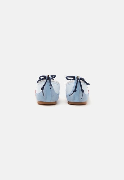 Paire de chaussures décontractées bleu clair et blanches avec des lacets bleu marine et des semelles marron, vues de dos sur un fond uni.