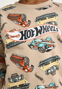 Beige sweatshirt met kleurrijke Hot Wheels autobedrukken. Ronde hals, lange mouwen, met een zachte textuur en levendige graphics overal.