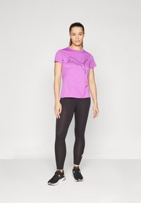 Camiseta atlética morada con el logo negro de Puma, combinada con leggings negros y zapatillas negras con acentos rosas. Diseño simple y ajustado.