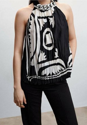 Femme portant un haut dos nu noir et blanc avec un motif abstrait audacieux et un pantalon noir, debout devant un fond uni.