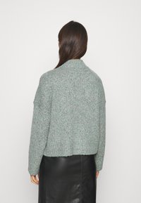 Suéter de punto verde claro con diseño corto, dobladillo acanalado y superficie texturada, usado sobre una falda de cuero negra.