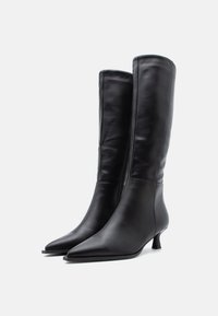 Bottes en cuir noir, hauteur genou, avec un bout pointu et un petit talon. Texture lisse avec un détail de fermeture éclair à l'arrière.