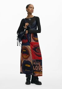 Vestito lungo con motivo grafico di labbra colorate, dettagli in metallo argentato e top nero aderente a maniche lunghe. Abbinato a una borsa nera e stivaletti.