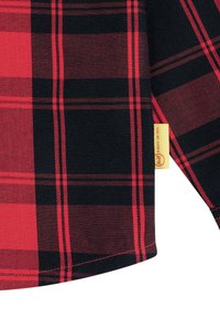 Camicia a quadri rossa e nera con una consistenza morbida, caratterizzata da linee prominenti in un motivo a scacchi. Include un piccolo cartellino beige sulla cucitura.