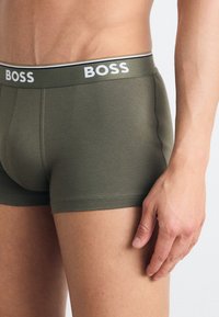 Olivengrønne boxershorts med en hvid talje med "BOSS" logo. Blødt stof, tætsiddende pasform, med en glat tekstur og minimale syninger.
