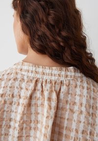 Blouse à carreaux pêche et blanc avec un encolure à l'arrière froncée, fabriquée en tissu texturé léger, arborant des rayures horizontales et verticales.
