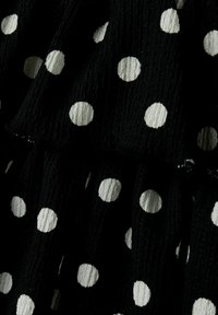 Zwarte gestructureerde stof met witte stippen, voorzien van gerimpelde lagen en een licht gekreukt oppervlak.