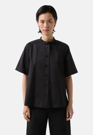 Černá krátká košile s mandarin límcem a předními knoflíky. Vyrobena z hladké tkaniny, disponuje volným střihem a minimalistickým designem.