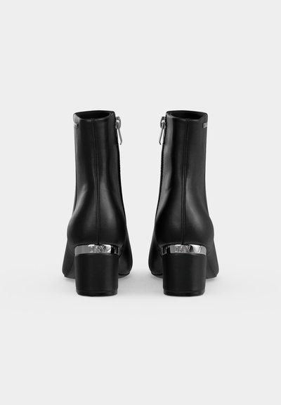 Bottines en cuir noir à talons blocs, fermetures éclair au dos et détail argenté gravé « DKNY », vues de dos sur fond blanc.