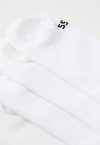 Calcetines de algodón blancos con una textura suave, que presentan un pequeño "55" negro bordado en el lado, apilados ordenadamente con un ligero solapamiento.
