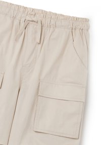 Beige cargoshorts met een elastische tailleband, trekkoord, twee zijzakken en twee grote opgestikte zakken aan de voorkant. Gladde textielafwerking.