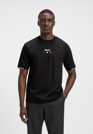 T-shirt nera a maniche corte in cotone, con collo rotondo, logo "BOSS" sopra tre accenti circolari colorati e dettagli a strisce sulle maniche.