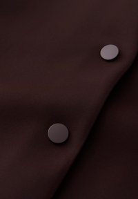Dark brown fabric with two round dark buttons placed diagonally on the cloth surface.
