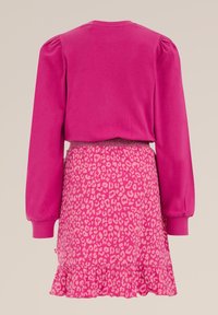 Růžový top s dlouhým rukávem a nabíranými rameny, spárovaný s růžovou sukní s leopardím vzorem a volánky na spodním lemu. Hladká textura po celé ploše.