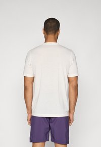 Hvit kortermet t-skjorte med rund hals, mykt stoff og rett nederkant, kombinert med lilla shorts. Ingen synlige mønstre eller detaljer.