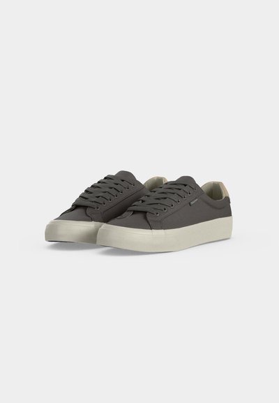 Paire de baskets basses gris charbon avec semelles épaisses en caoutchouc blanc et lacets gris assortis sur un fond clair uni.